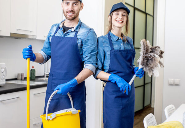 Portrait of a couple as a professional cleaners in uniform standing together with cleaning tools indoors
